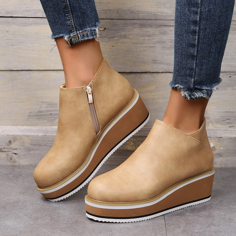 Tan wedge ankle boots worn with blue jeans on a wooden floor.