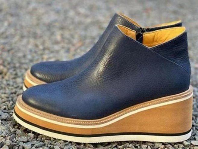 Pair of navy blue wedge ankle boots with brown soles on a textured surface